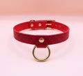 A red leather choker collar with a gold-colored metal ring and buckle.