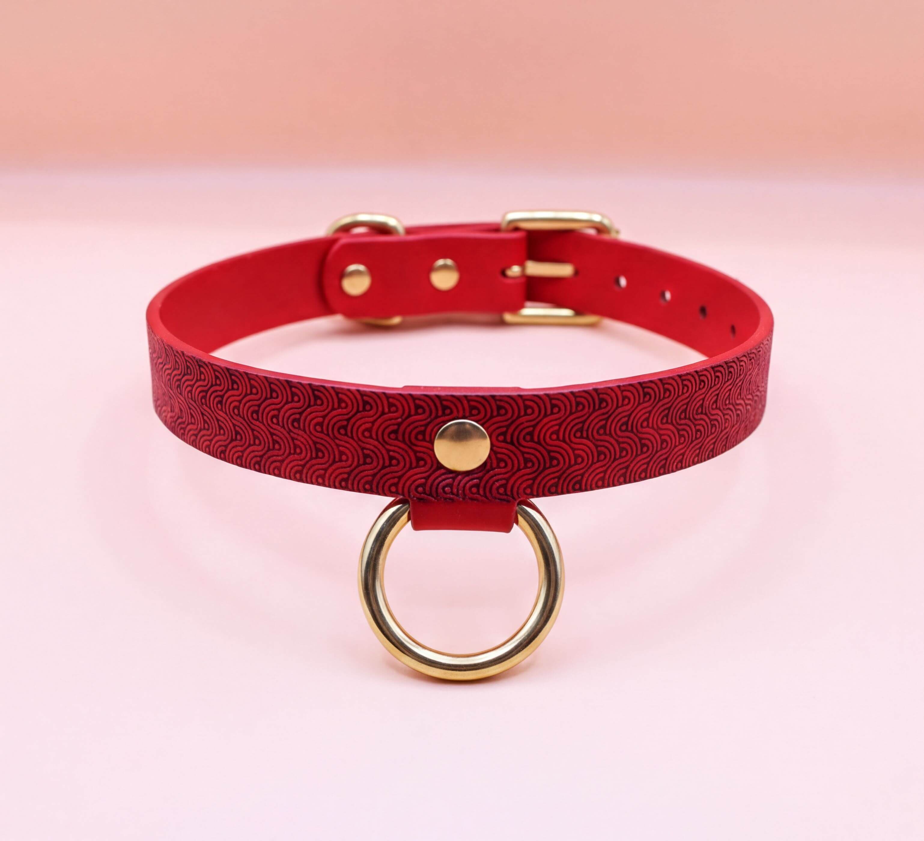 A red leather choker collar with a gold-colored metal ring and buckle.
