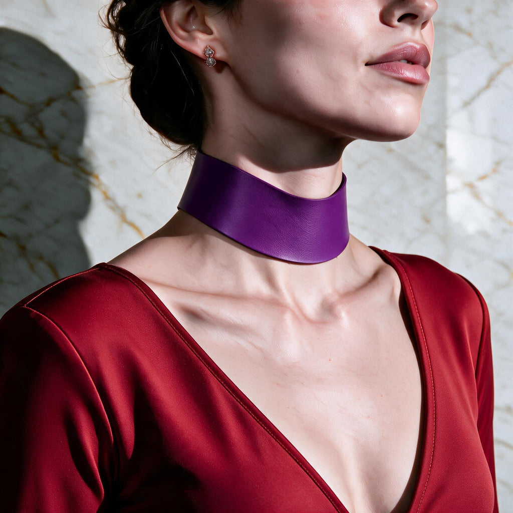 A woman wearing a red dress with a purple choker necklace stands against a marble wall.