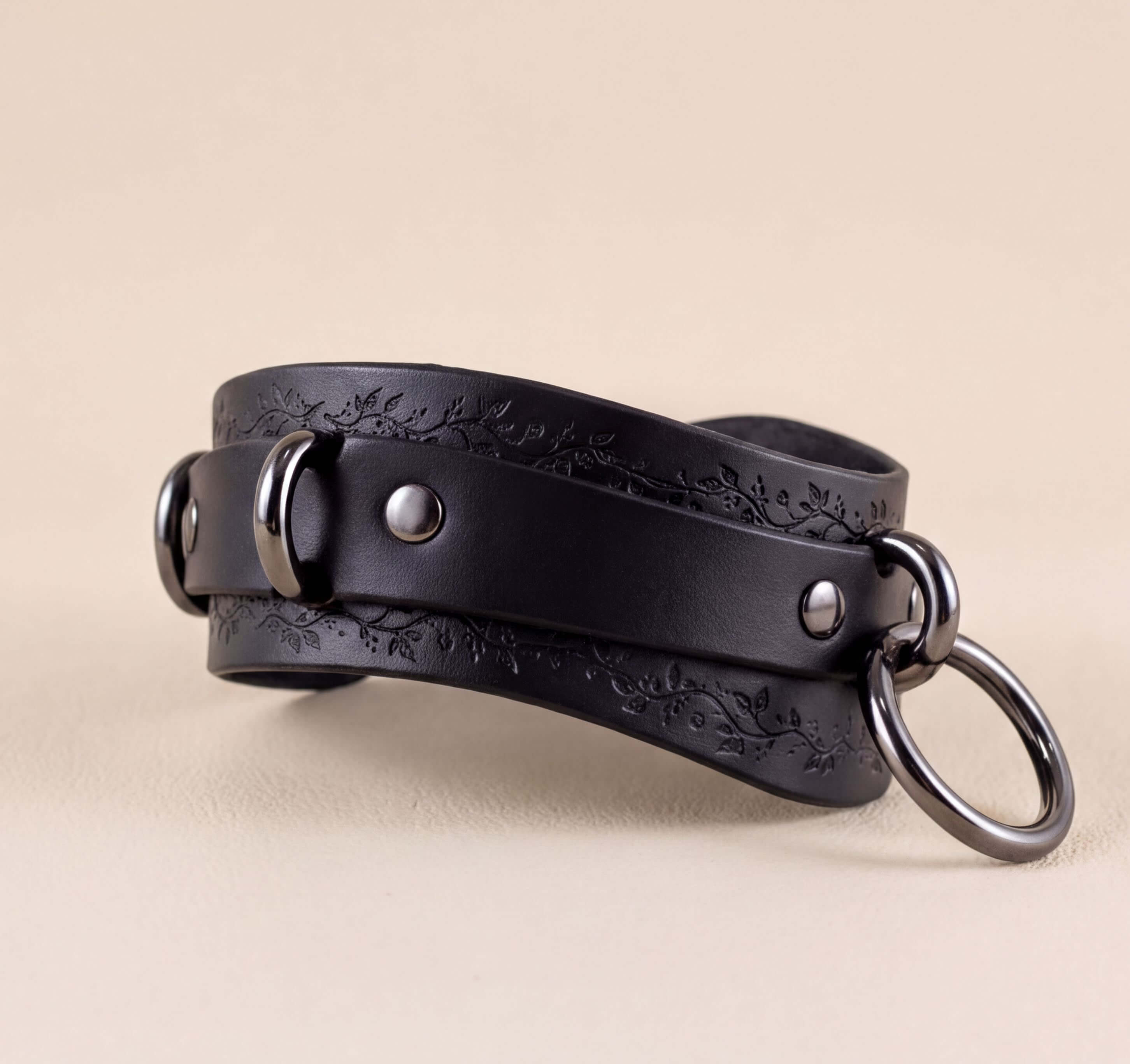 A black leather choker with metal rings and a decorative pattern on the straps.