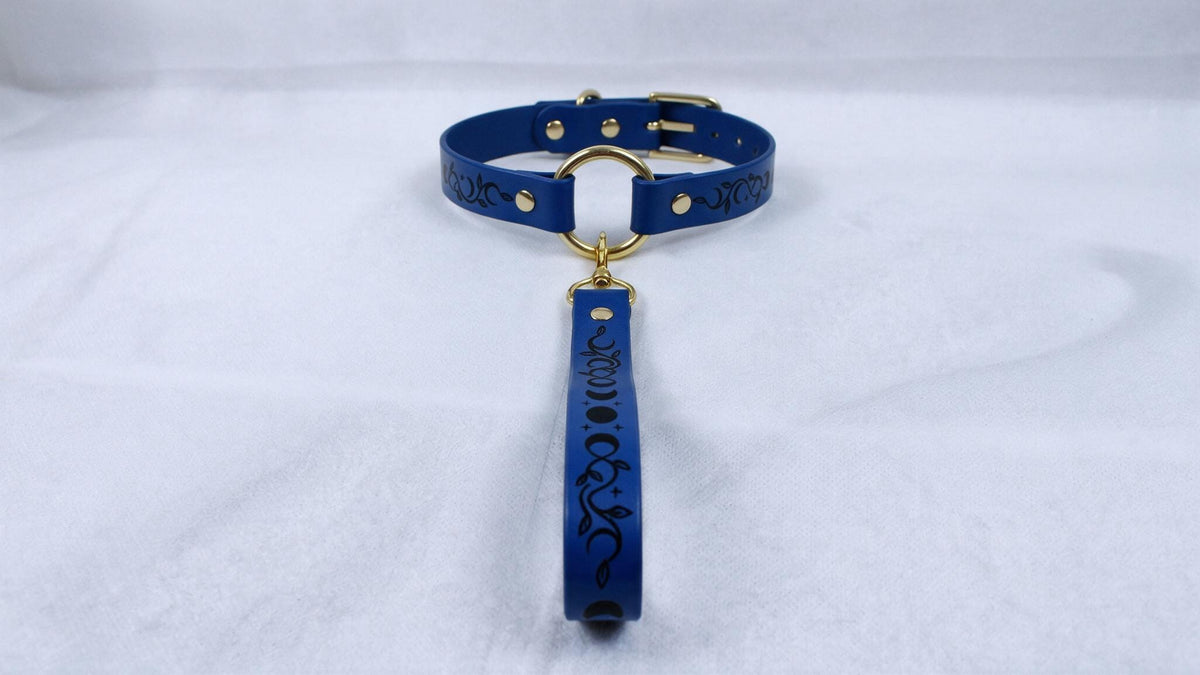 A blue collar with a gold buckle and a black handle attached to it, placed on a white surface.