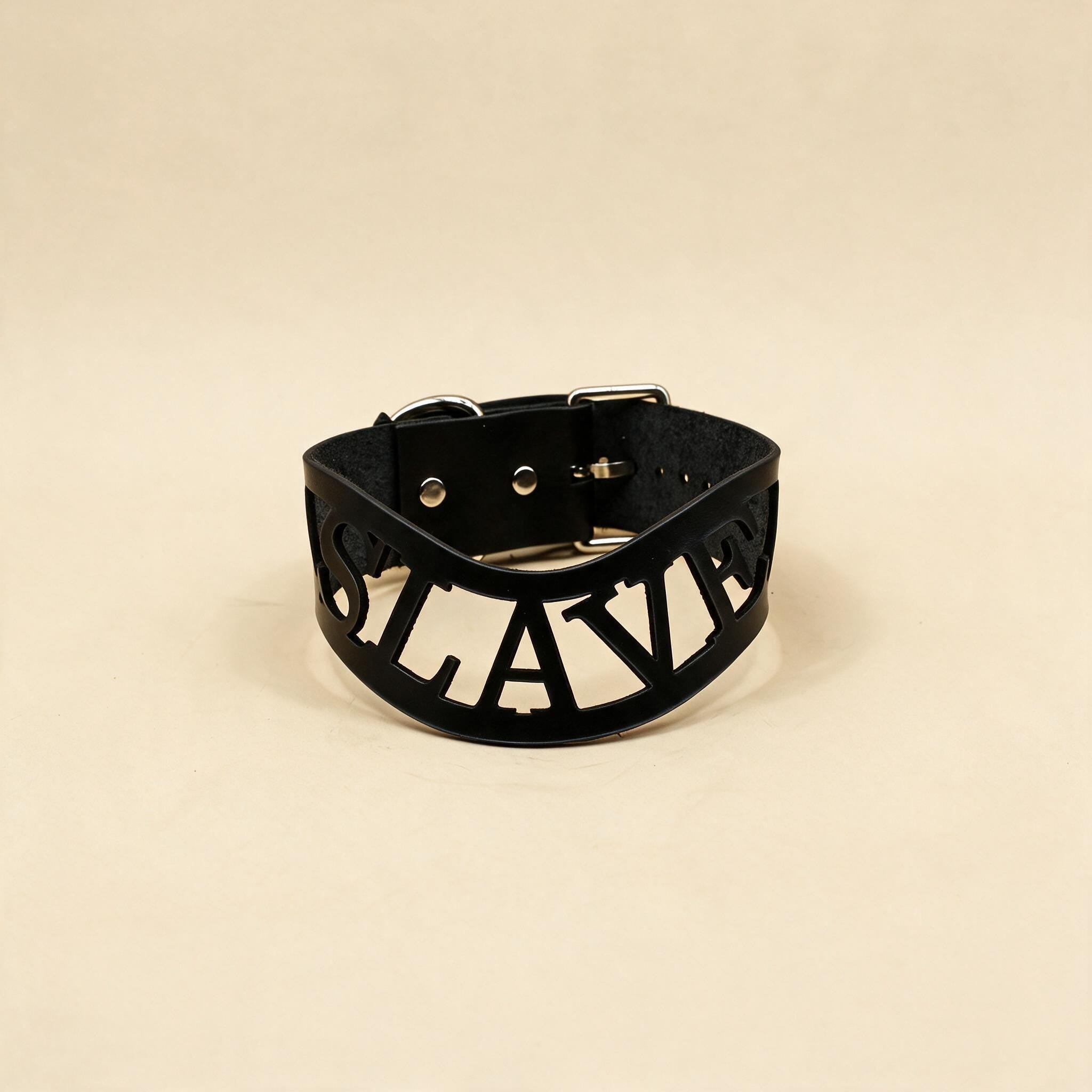 A black leather choker necklace with the word "SLAVERY" printed on it in a bold, capitalized font.