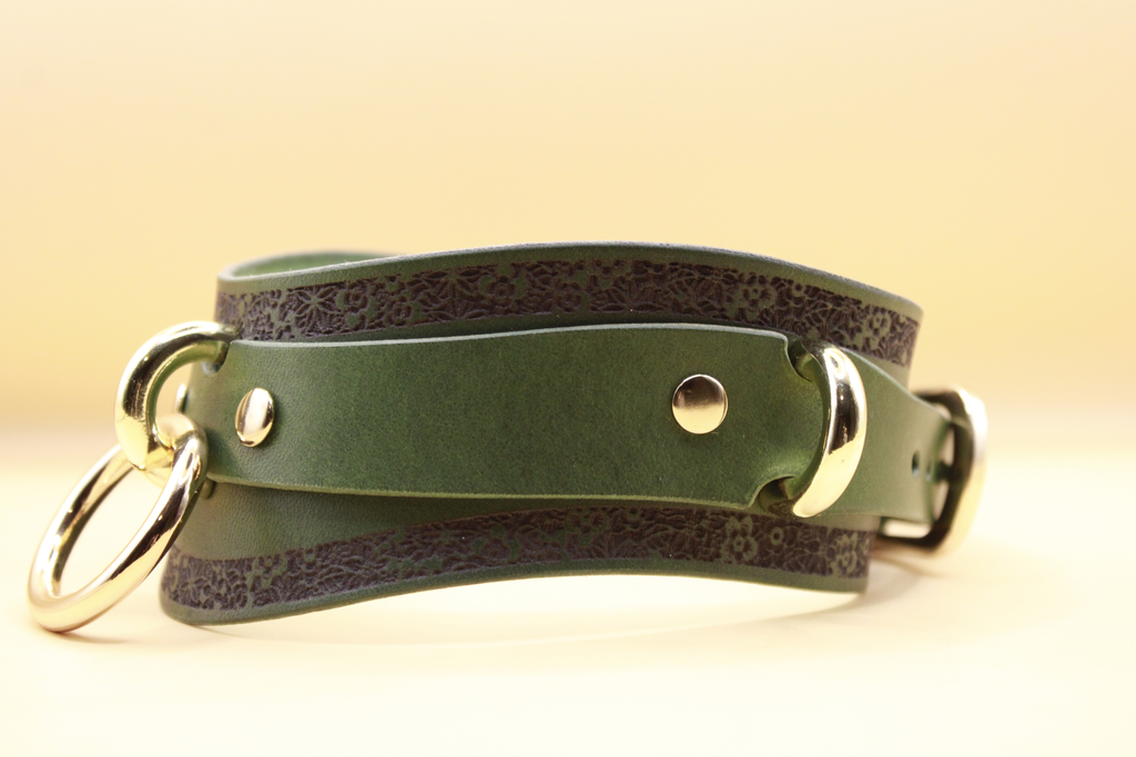 A green leather choker with metal rings and a decorative pattern on the edges.