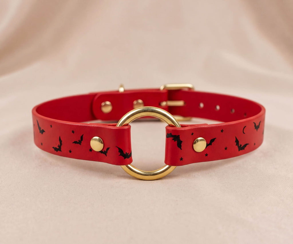 A red leather collar with a gold ring and black bat designs.