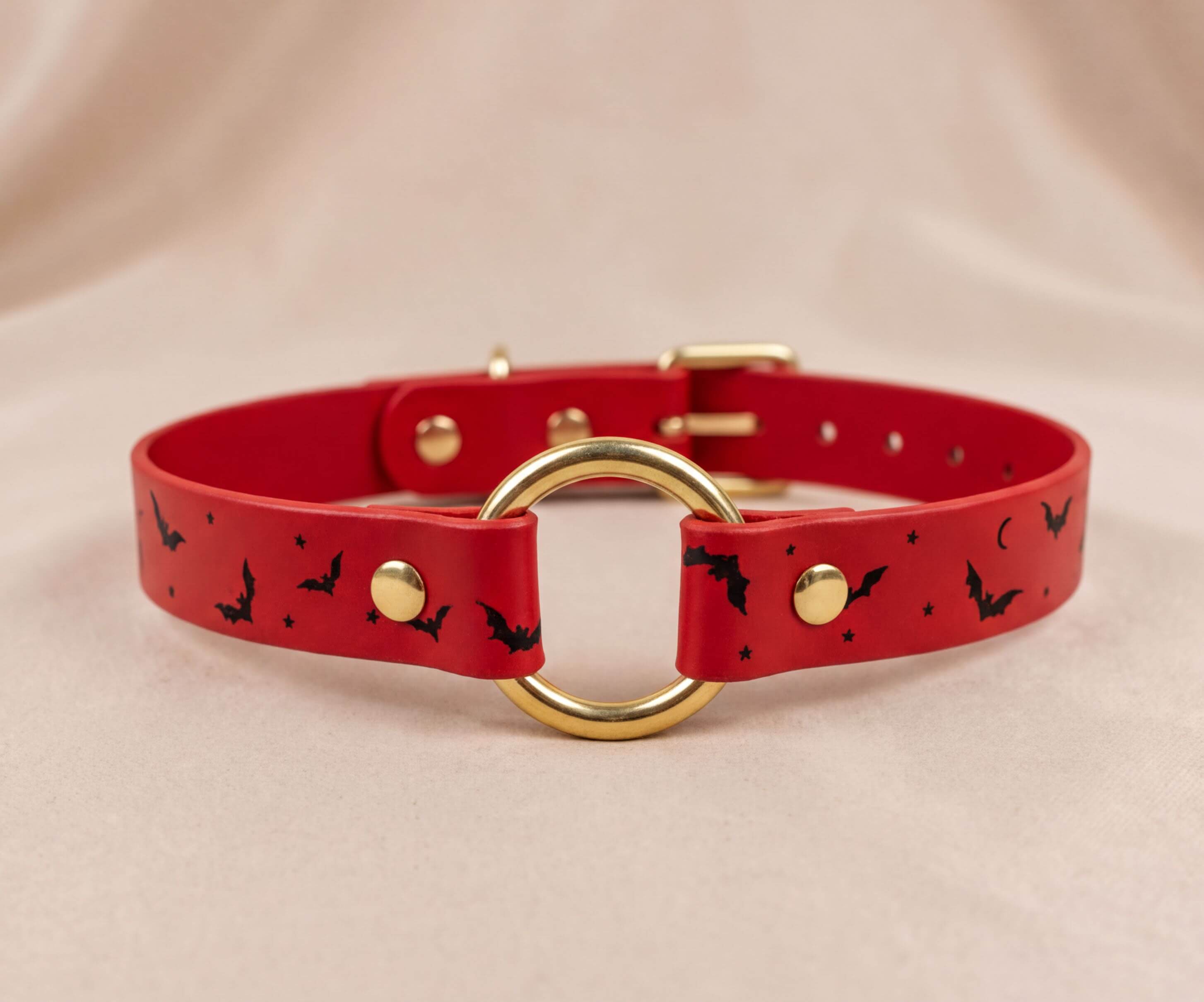 A red leather collar with a gold ring and black bat designs.