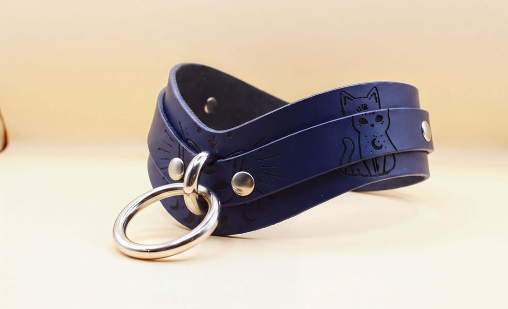 A dark blue leather choker necklace with a silver ring and a cat design on the front.