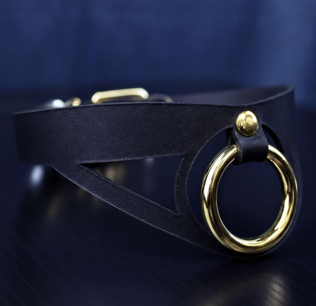 A close-up view of a black leather choker necklace with a gold-colored circular clasp.