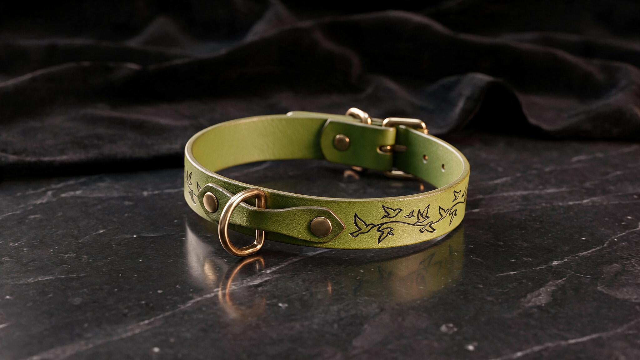 A green leather collar with a bird design on it, placed on a black marble surface.