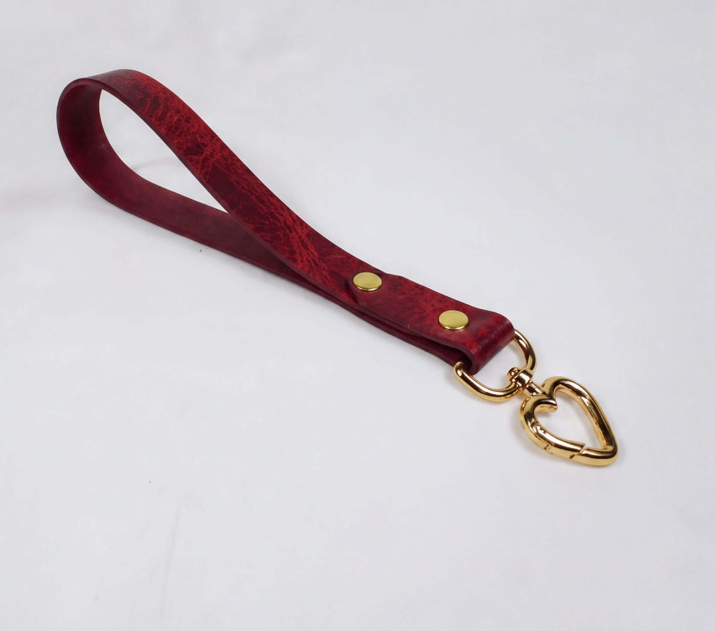 A red leather strap with a heart-shaped metal clasp attached to it, resting on a white surface.