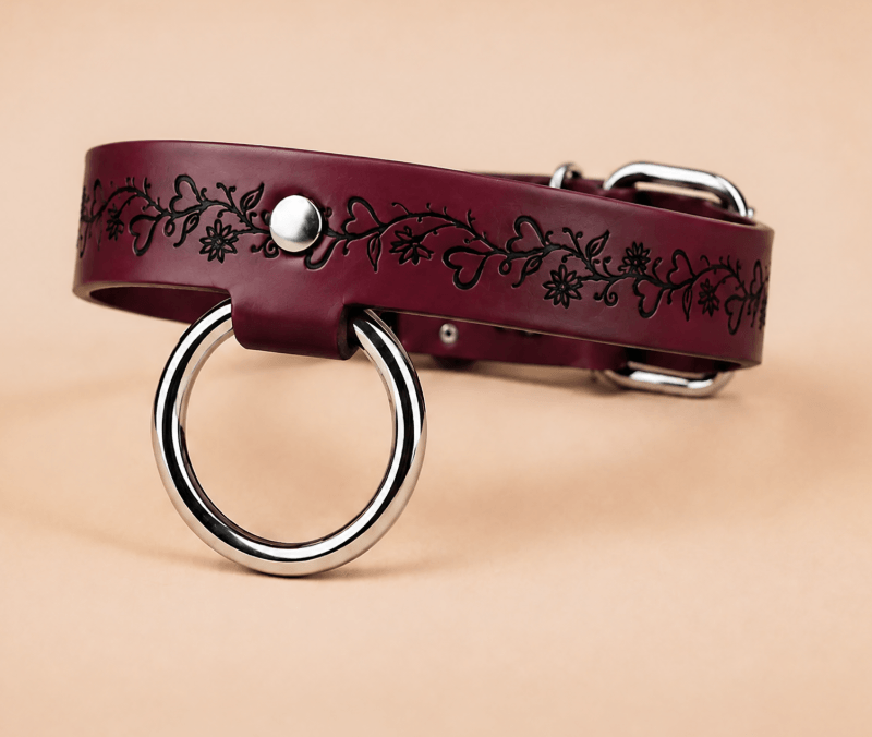 A burgundy leather collar with a metal ring and floral design on the strap.