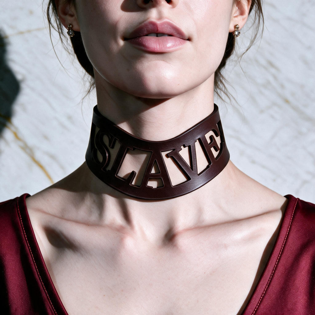 A close-up of a woman wearing a large, dark-colored choker necklace with the word "SLAVE" prominently displayed on it.