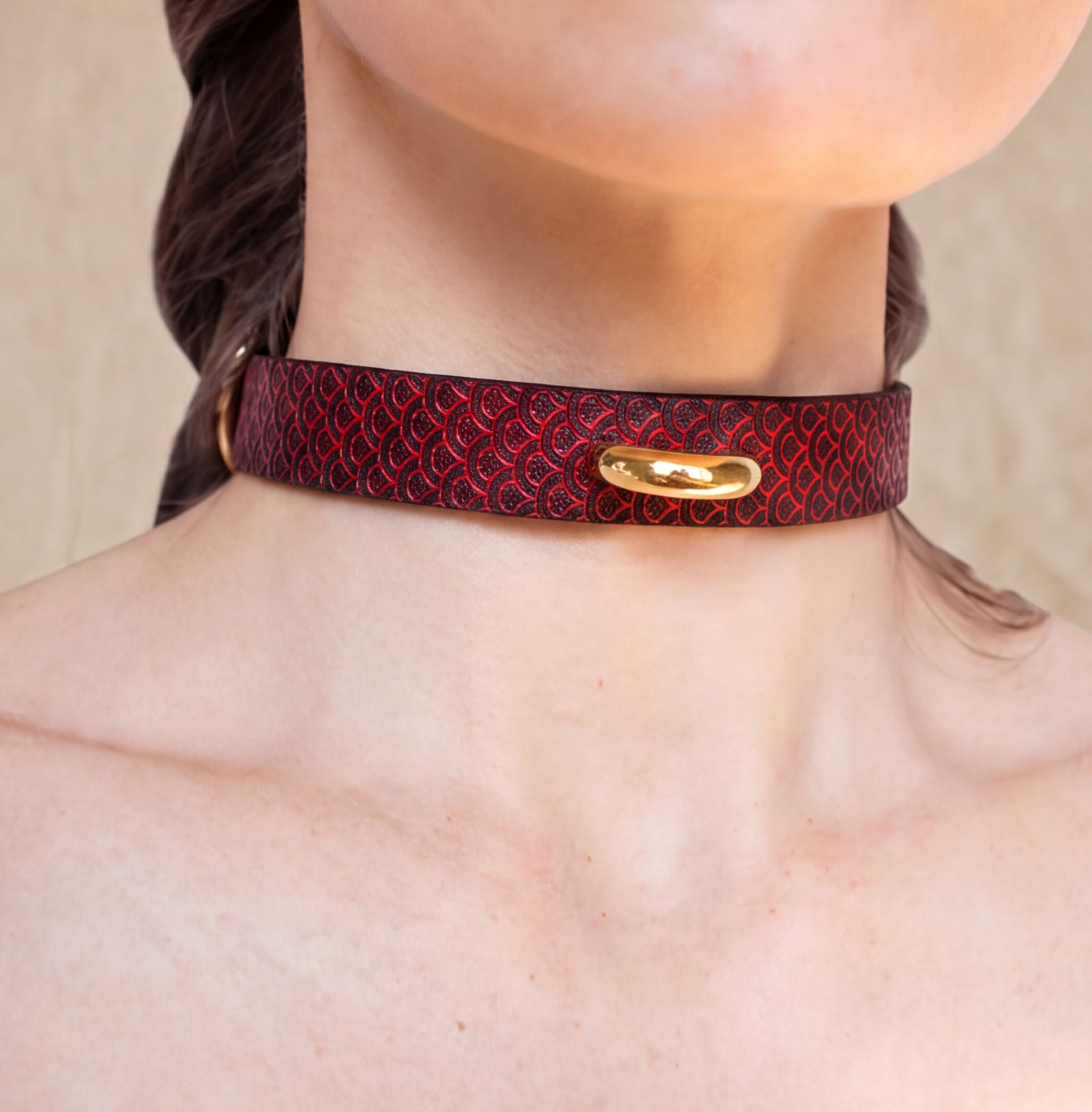 A close-up of a person's neck wearing a red and black patterned choker necklace with a gold-colored clasp.