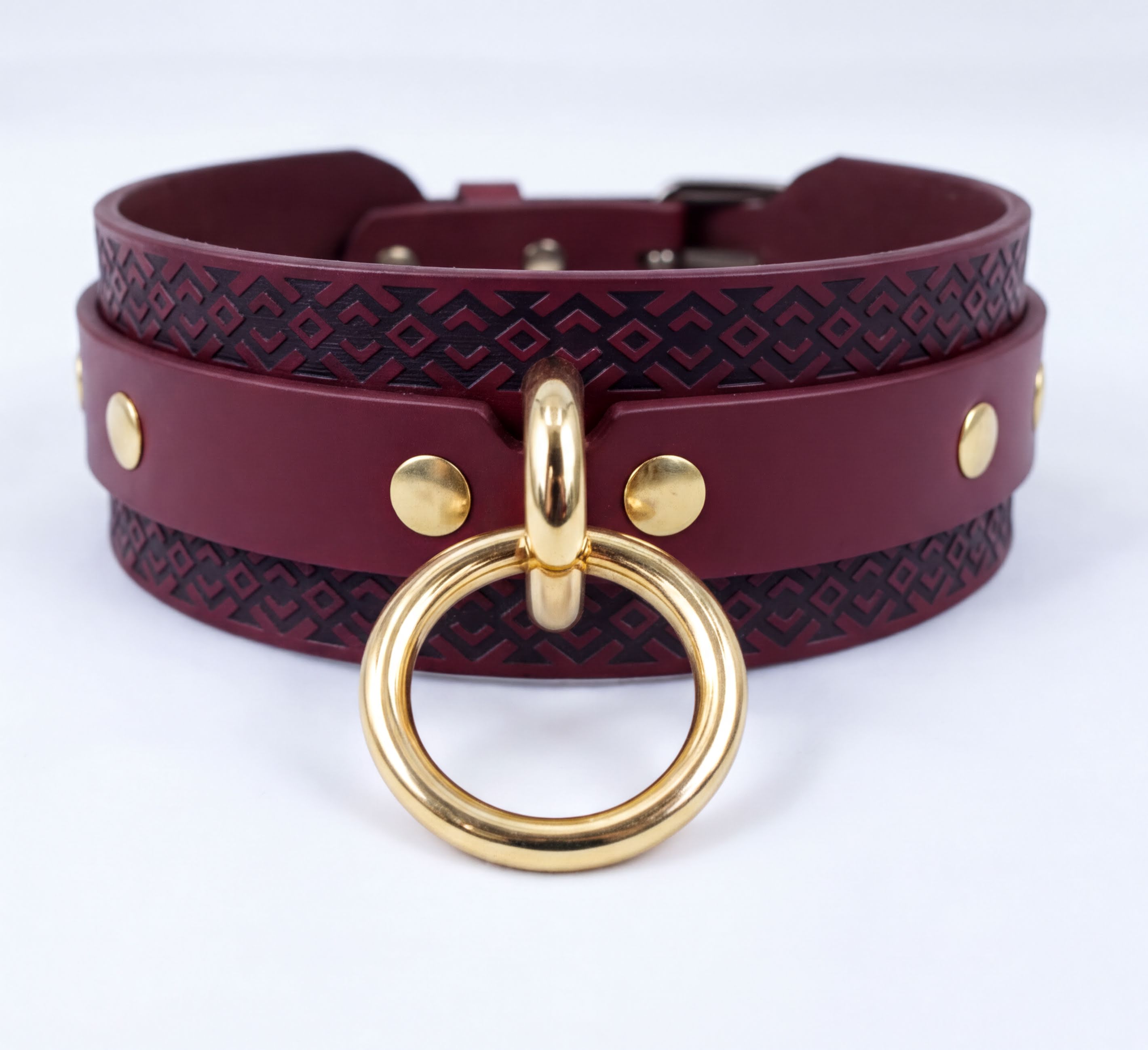 A burgundy leather choker necklace with a gold-colored metal ring and a decorative pattern on the band.