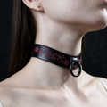 A close-up of a woman's neck and chin wearing a black choker necklace with a floral design.
