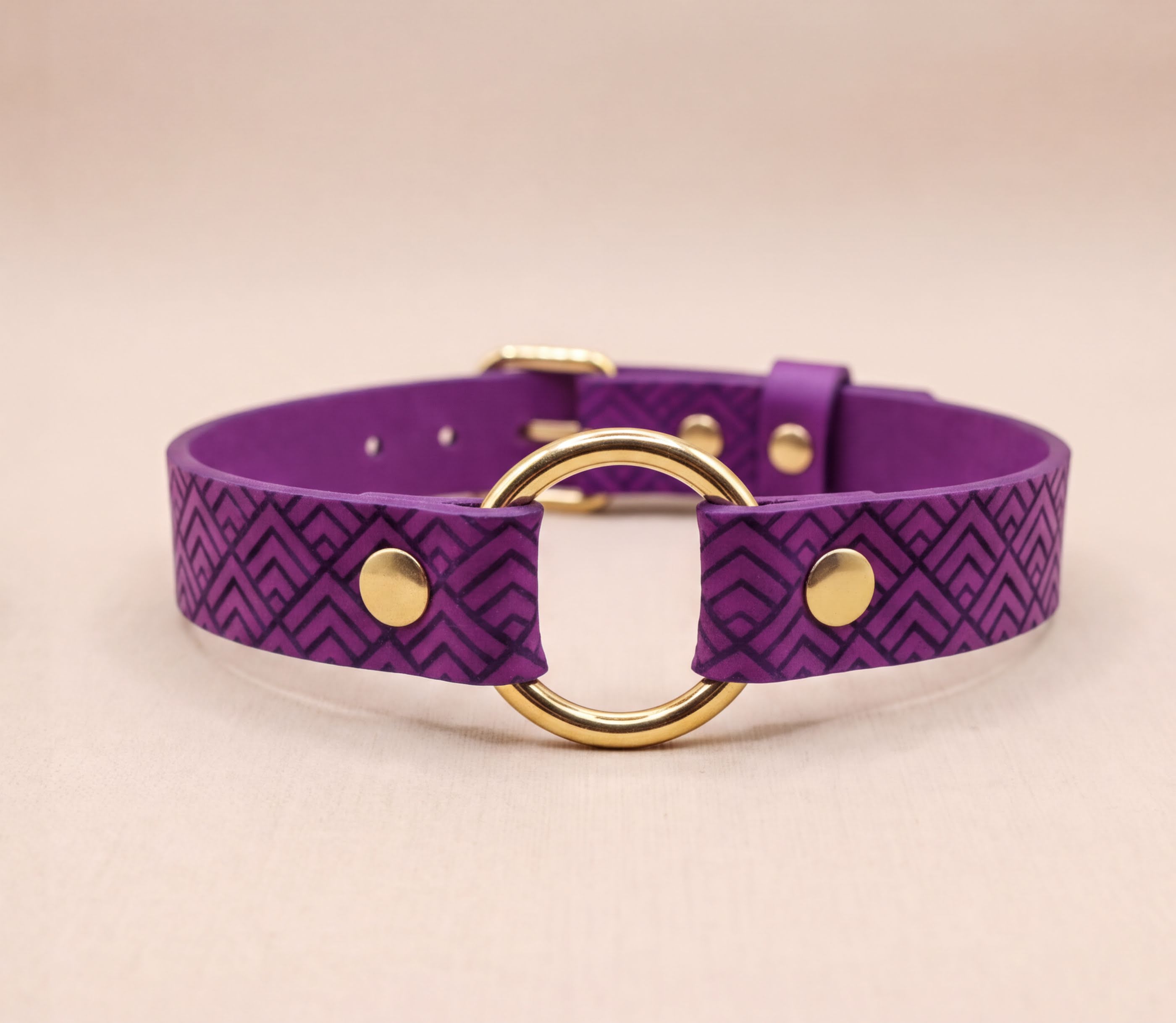 A purple leather collar with a gold-colored circular buckle.