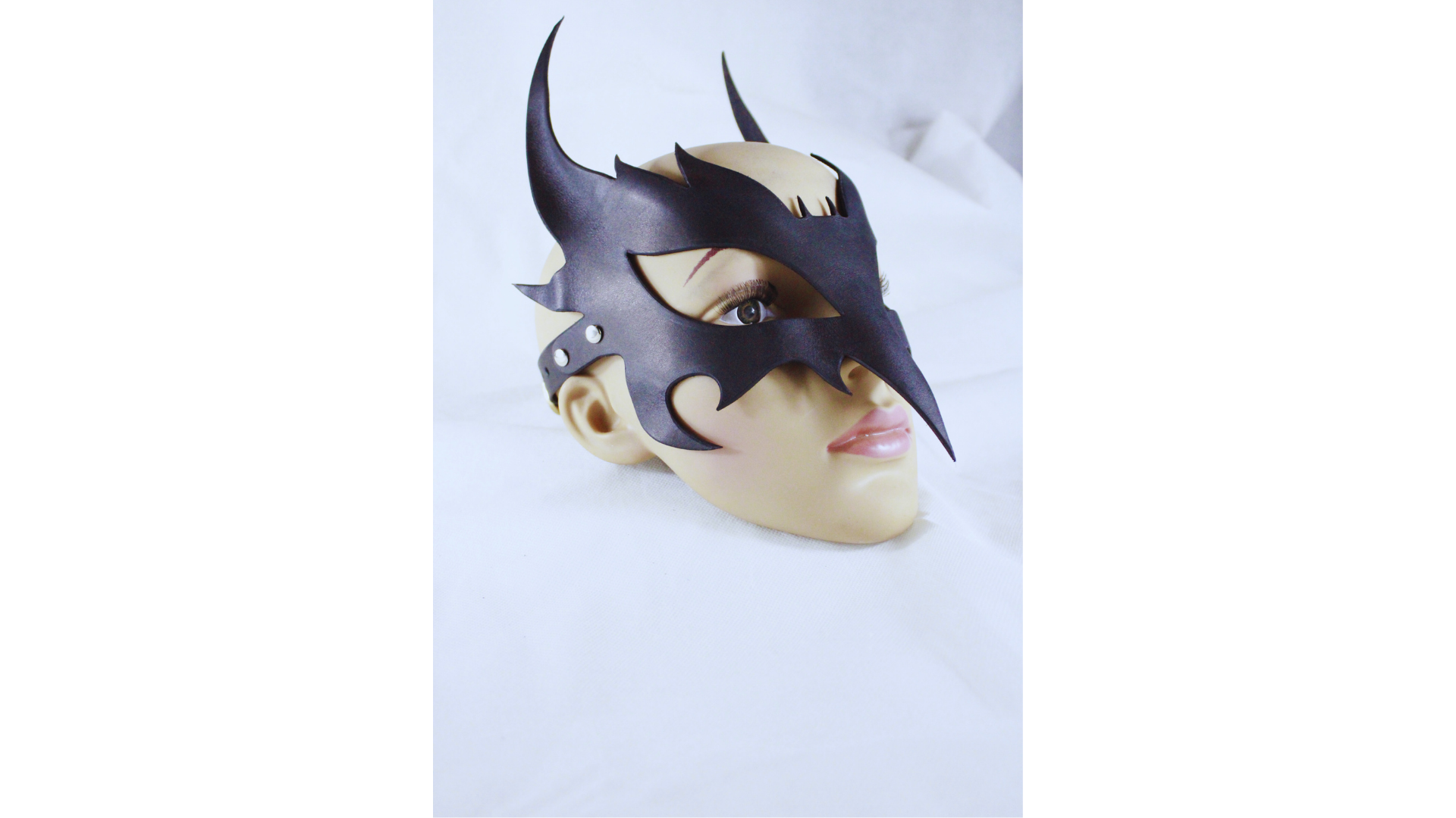 A mannequin head wearing a black mask with sharp horns and a pointed nose, set against a white background.