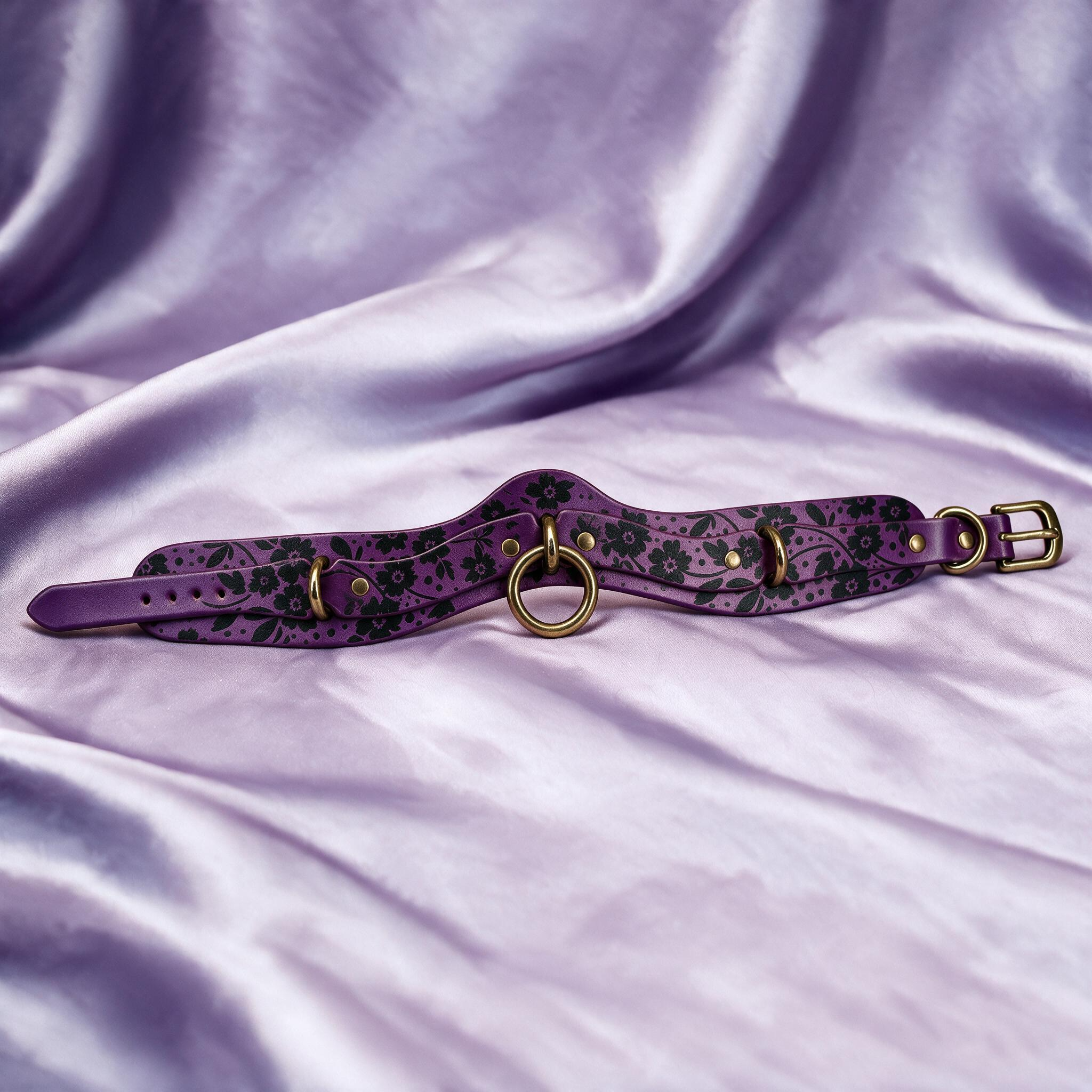 A purple choker collar with floral patterns and metal rings is displayed on a purple satin background.