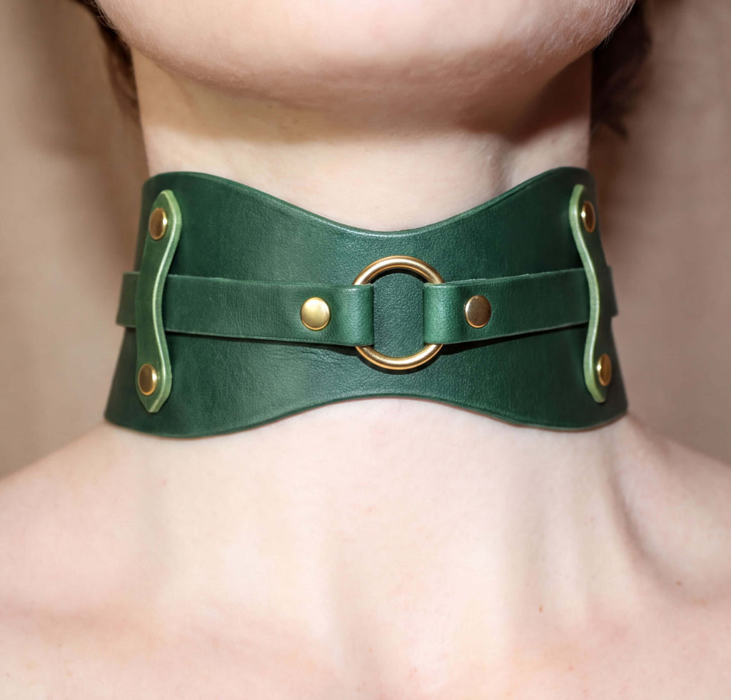 A close-up view of a person's neck and chest area wearing a green leather choker necklace with a gold-colored metal ring.