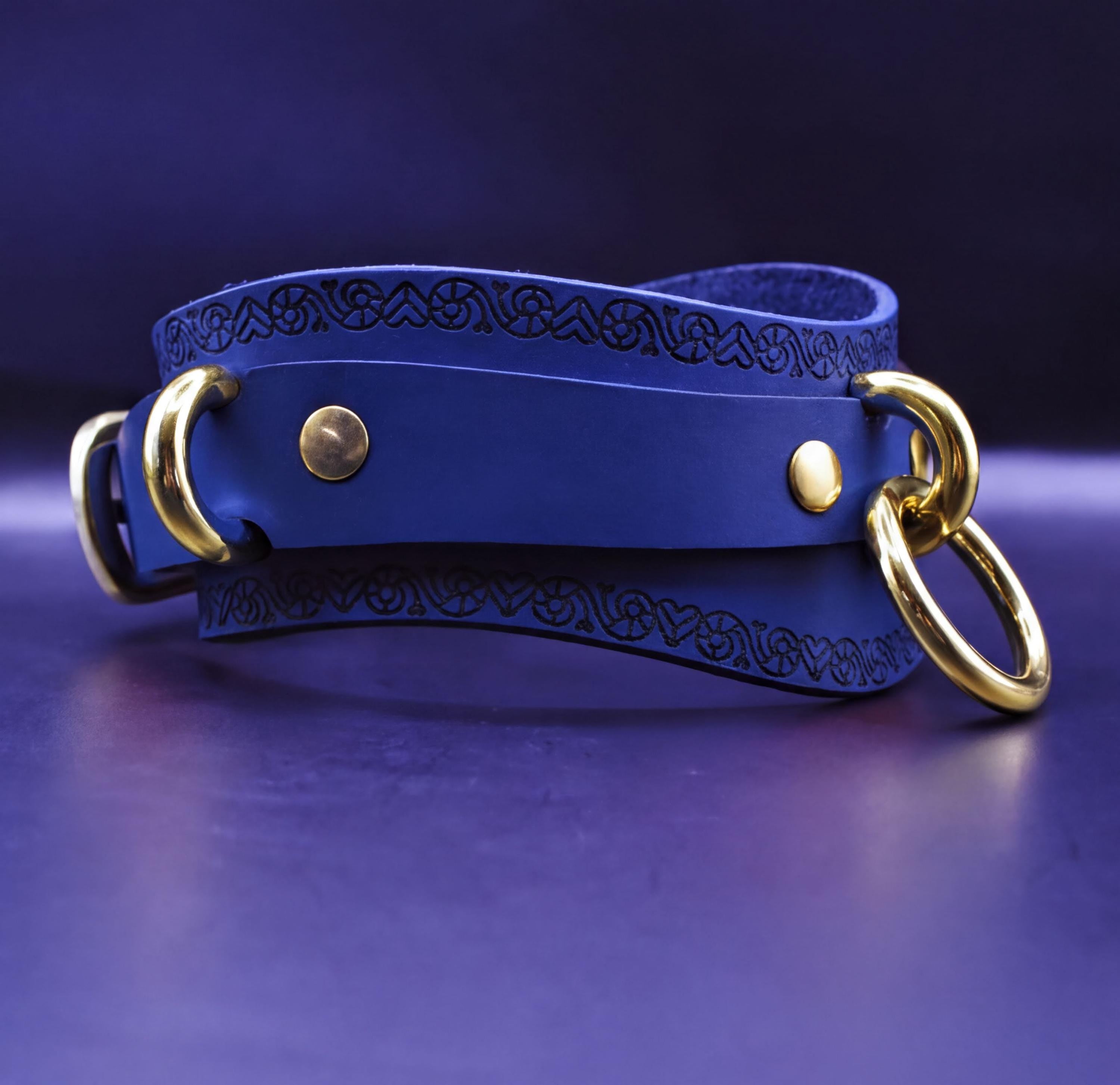 A blue leather choker necklace with gold-colored metal rings and a decorative pattern on the clasp.
