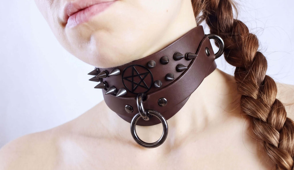 A close-up of a woman's neck wearing a leather choker necklace with spikes and a pentagram symbol.