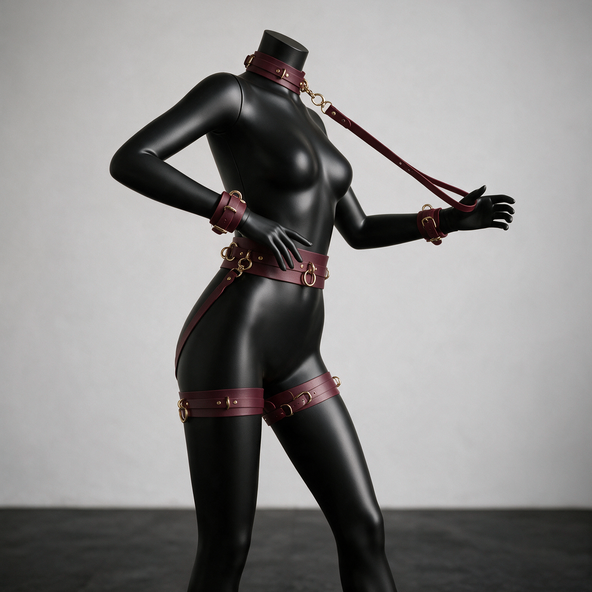 A mannequin wearing a black leather outfit with red straps and accessories, posing in a studio setting.