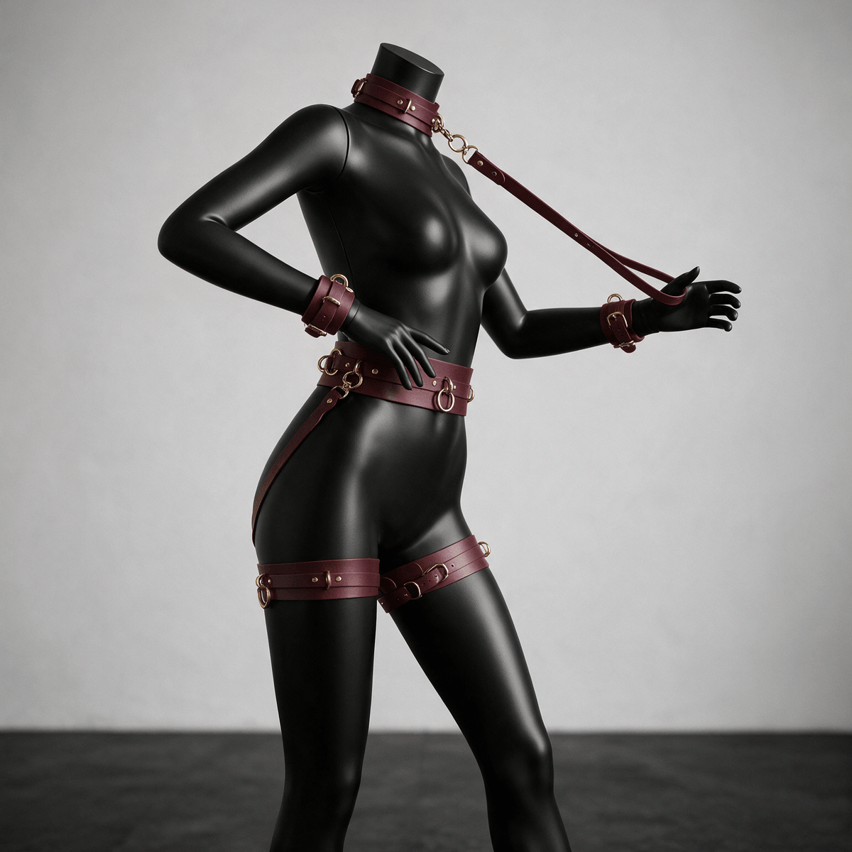 A mannequin wearing a black leather outfit with red straps and accessories, posing in a studio setting.