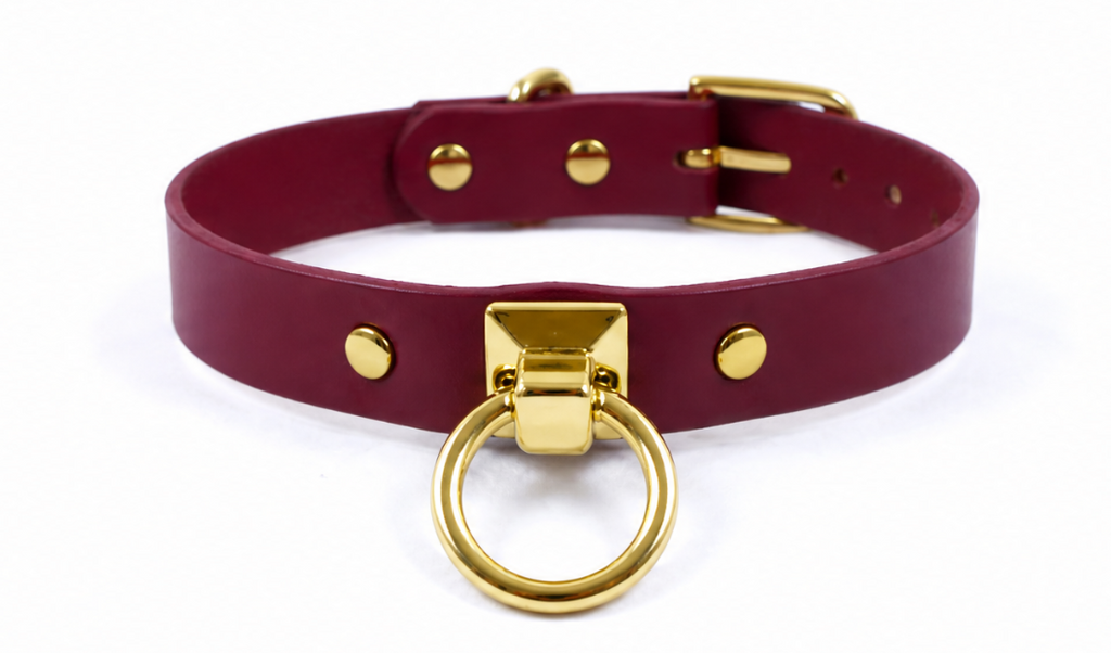 A burgundy leather choker collar with a gold metal ring and buckle.