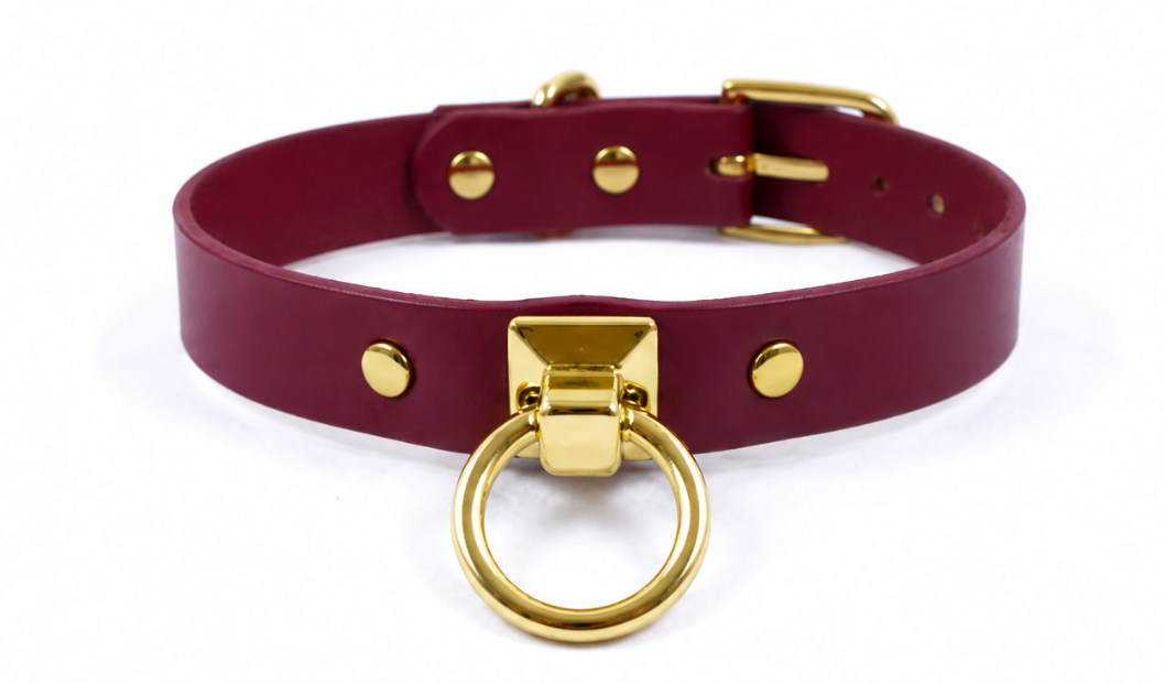 A burgundy leather choker collar with a gold metal ring and buckle.