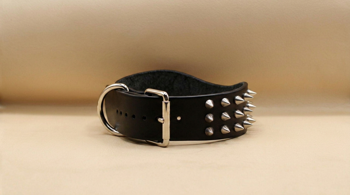 A black leather belt with silver spikes protruding from it, resting on a beige background.