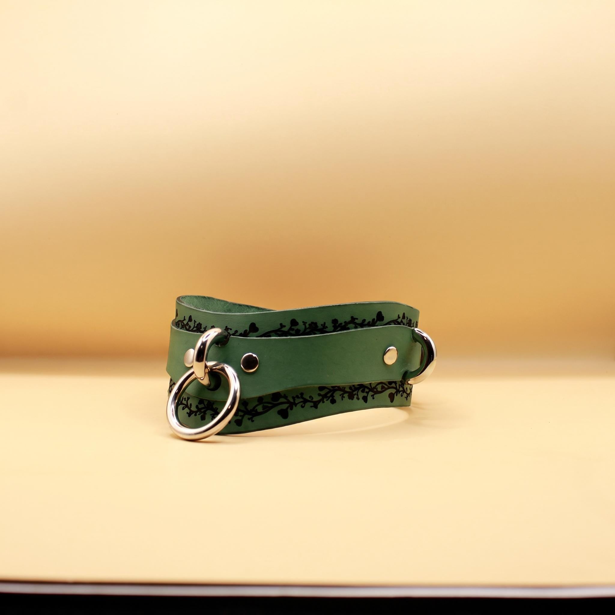 A green leather choker necklace with metal rings and a decorative pattern on the leather.