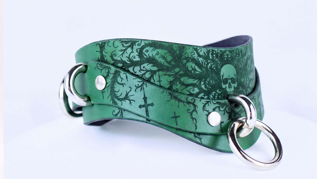 A green leather choker necklace with a skull design and metal rings.