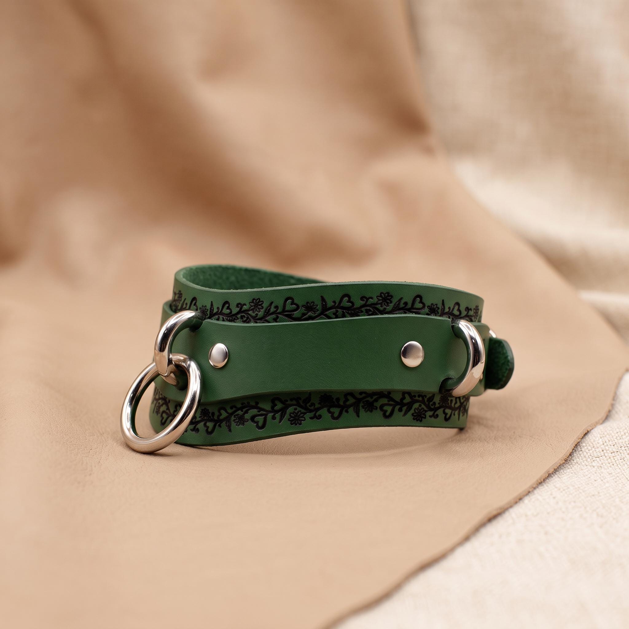 A green leather choker necklace with metal rings and a decorative pattern on the leather.