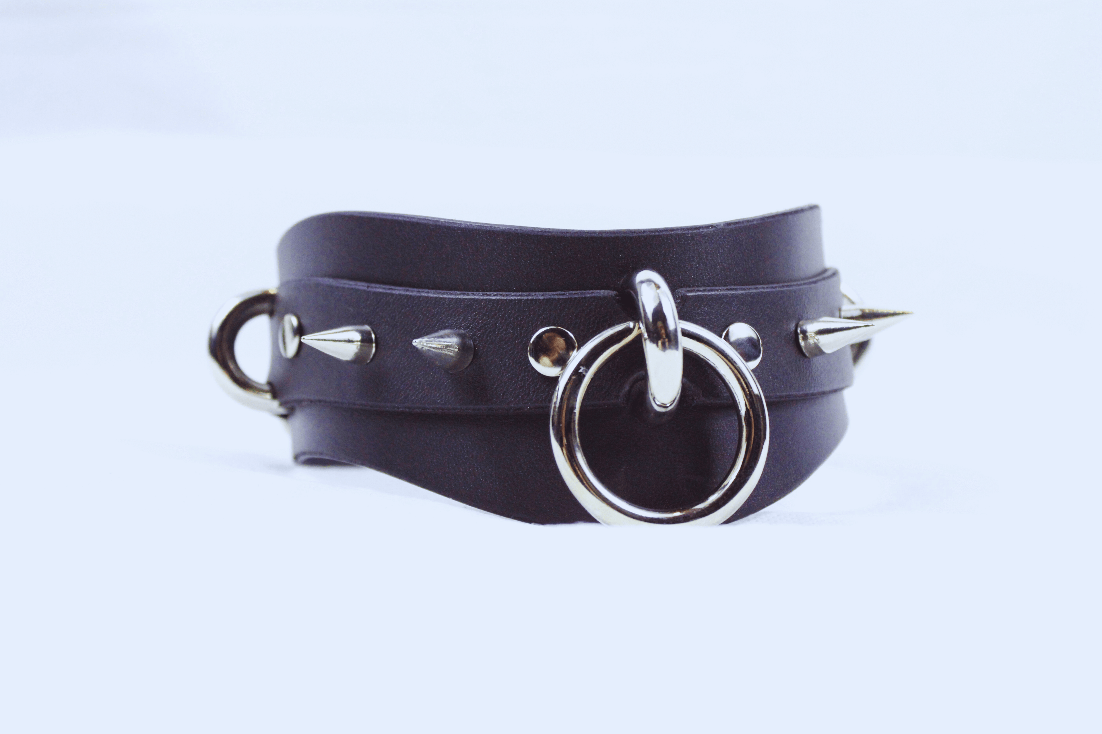 Getoogde BDSM Halsband Met Spikes in zwart leer met metalen O-ringen en spikes.