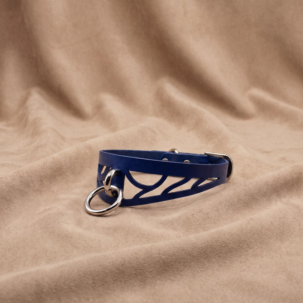 A blue leather choker necklace with metal rings and a metal buckle is displayed on a beige fabric background.