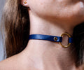 A close-up view of a person's neck and chin area, featuring a blue leather choker necklace with a gold-colored circular clasp.