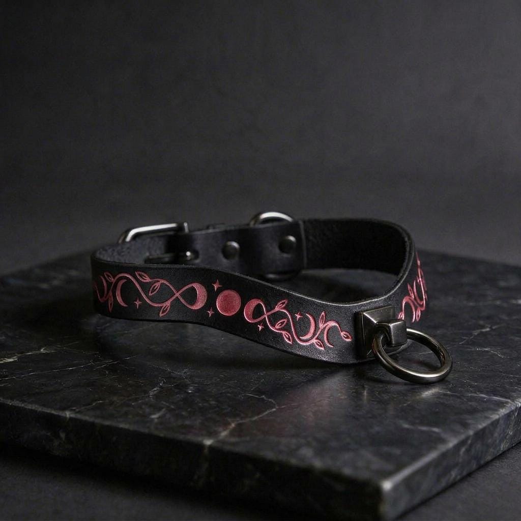 A black leather collar with a pink and red floral design on it, resting on a black surface.
