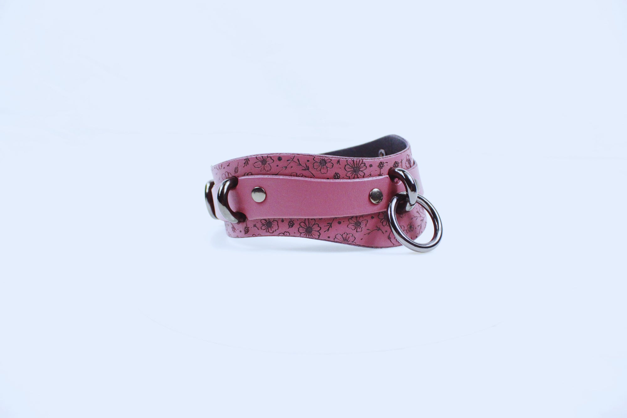 A pink leather collar with metal rings and a floral pattern.