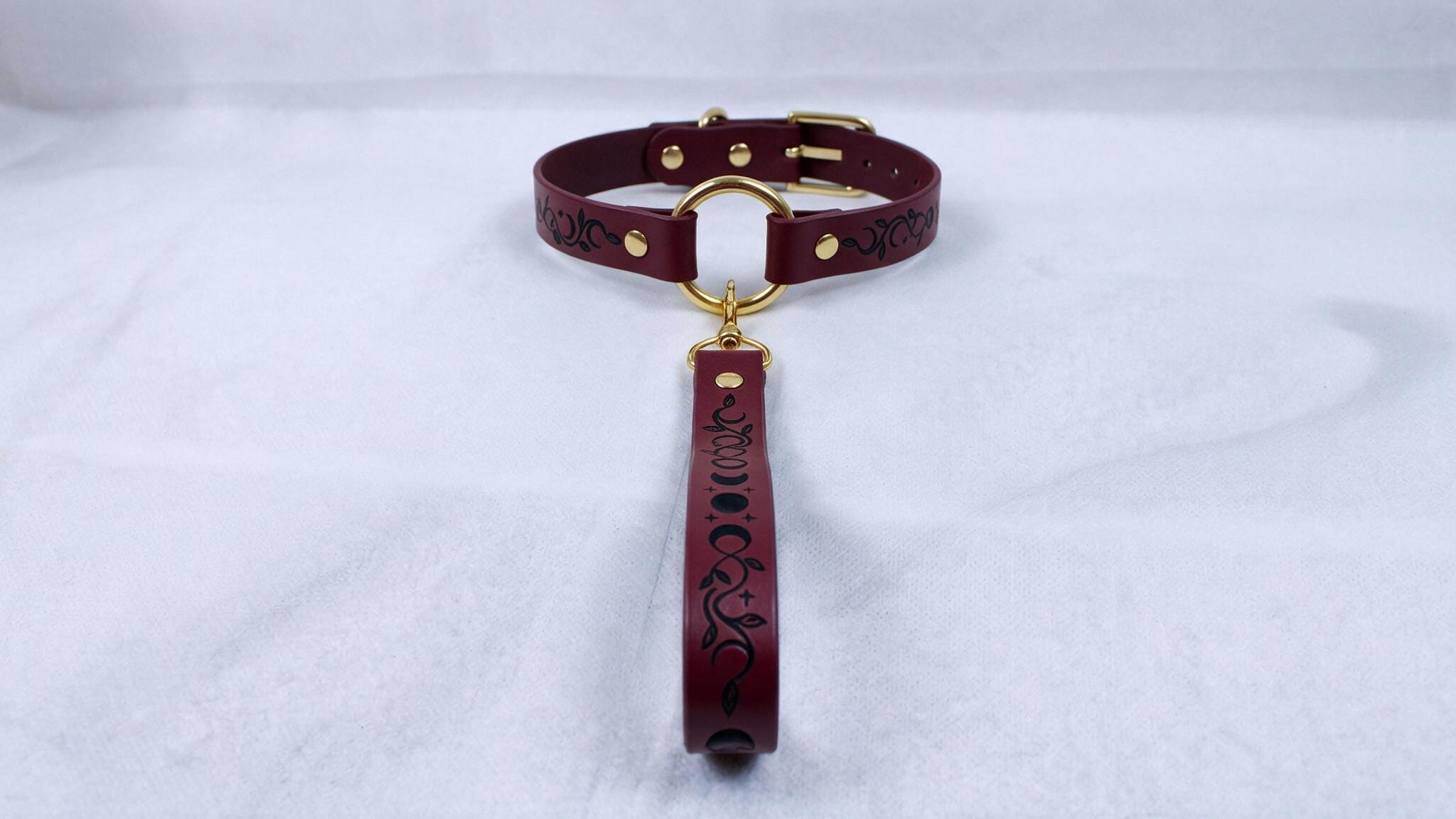 A burgundy leather collar with a gold buckle and a black and white floral pattern on the strap.