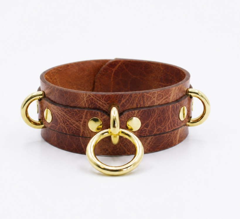 A brown leather choker necklace with gold metal rings and buckles.