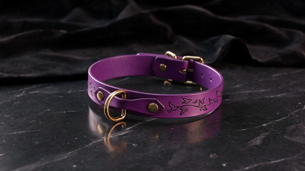 A purple leather collar with a gold-colored buckle and a floral design on the side, resting on a black marble surface.
