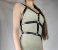 A woman wearing a beige dress with a black leather harness and straps around her torso.