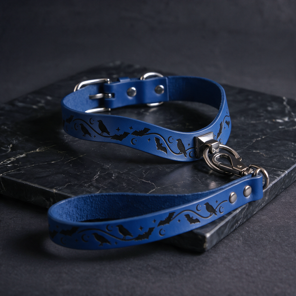 A blue leather dog collar with a bat and moon design, featuring a silver buckle and a black handle, is displayed on a dark surface.