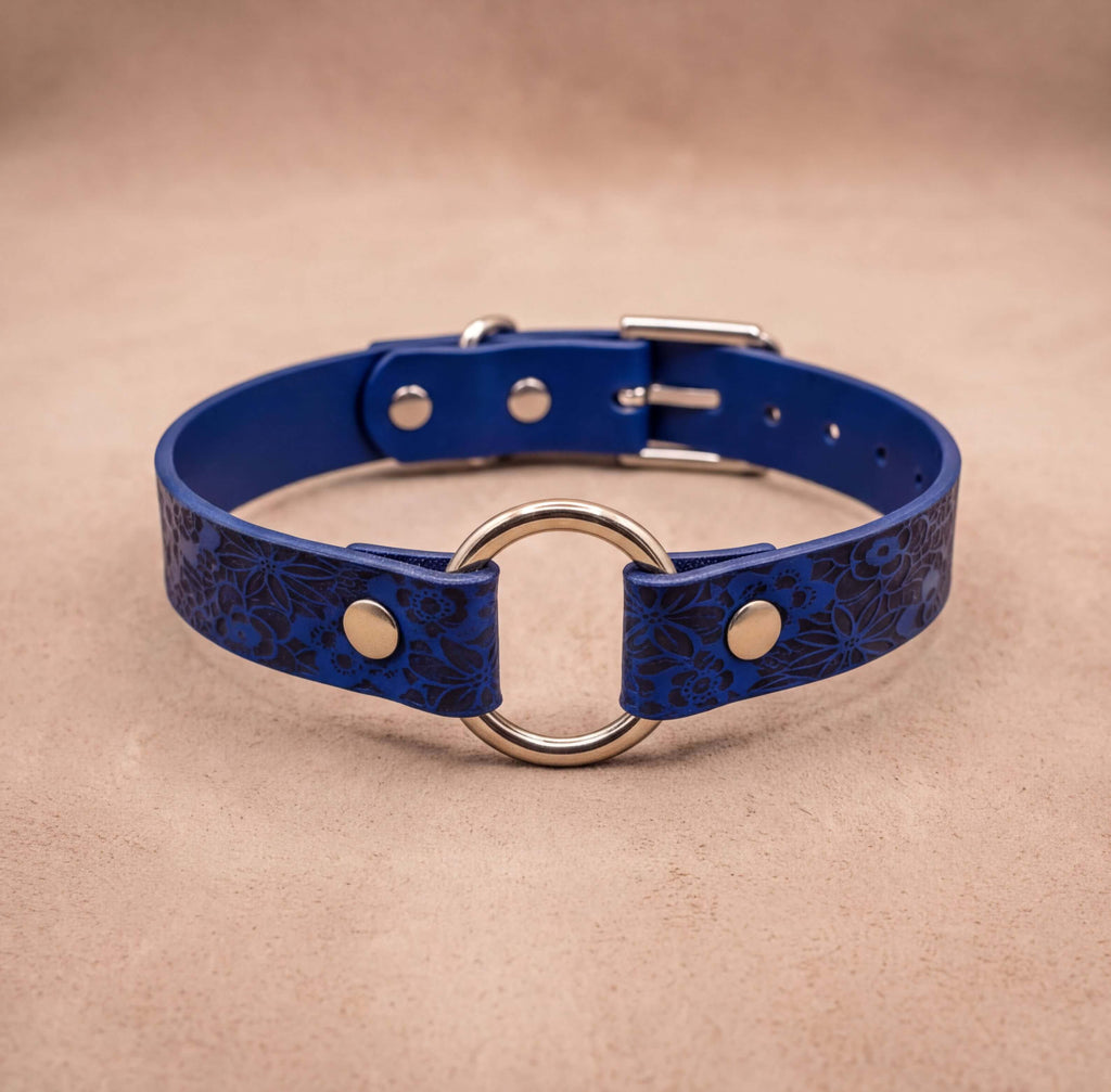 A blue leather collar with a metal ring and buckle, placed on a beige background.
