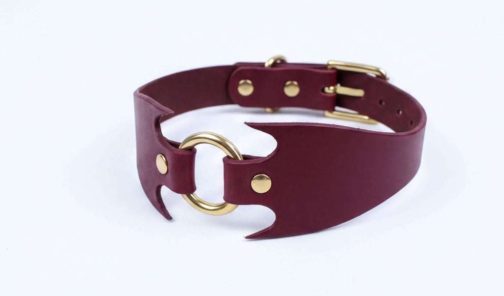 A burgundy leather choker necklace with a gold-colored buckle and a unique, angular design.