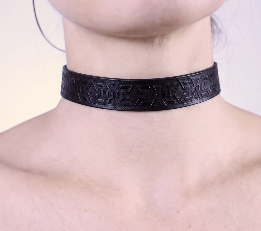 A close-up view of a person's neck and chest area wearing a black choker necklace with an intricate geometric pattern.