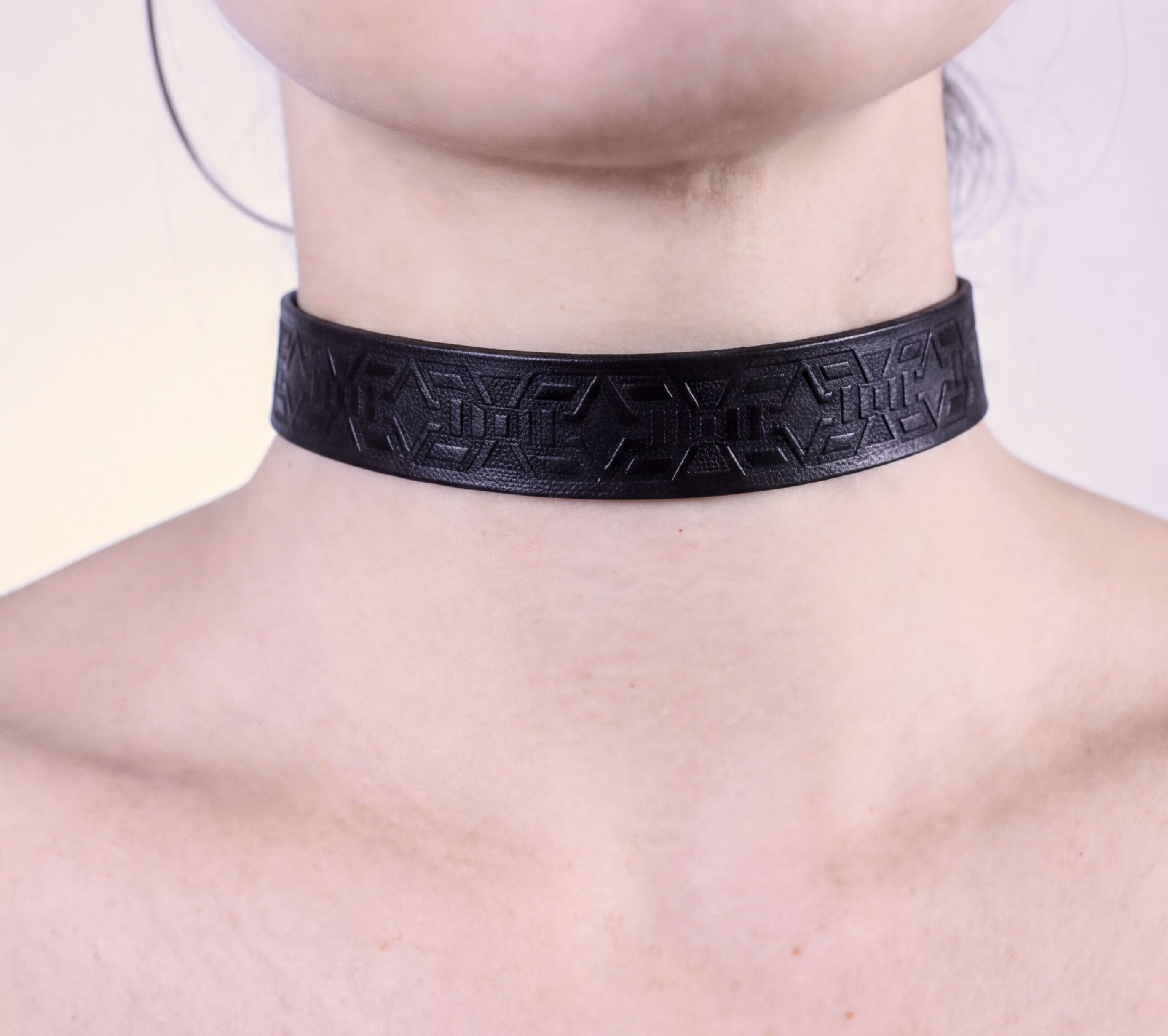 A close-up view of a person's neck and chest area wearing a black choker necklace with an intricate geometric pattern.