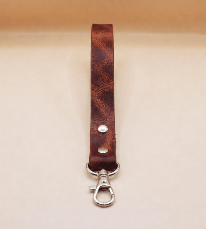 A brown leather strap with a metal clasp and hook attached to it.