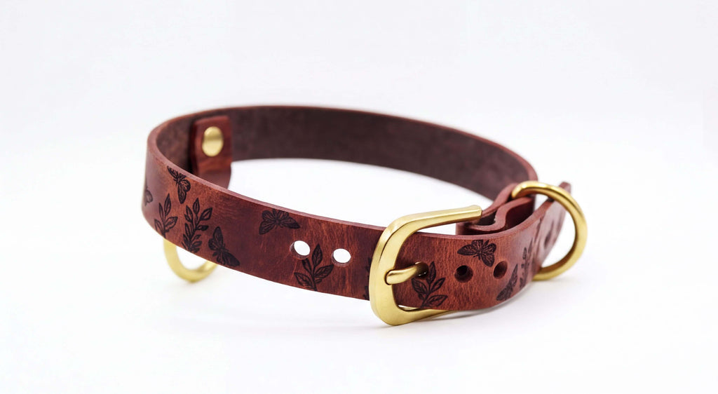 A brown leather dog collar with a gold buckle and a leaf pattern design.