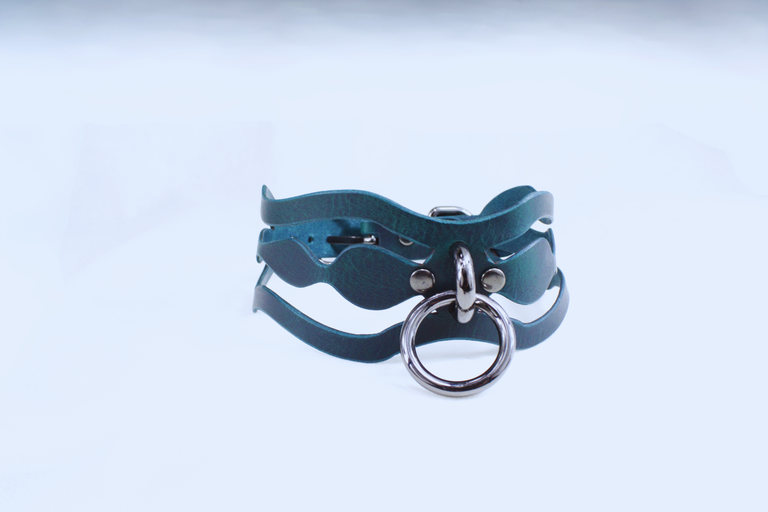 A dark blue leather bracelet with a metal ring and buckle, set against a white background.