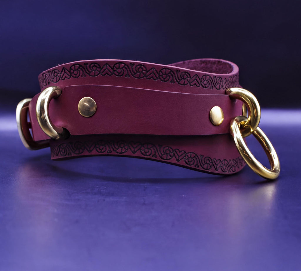 A burgundy leather choker necklace with gold-colored metal rings and a decorative pattern on the leather.